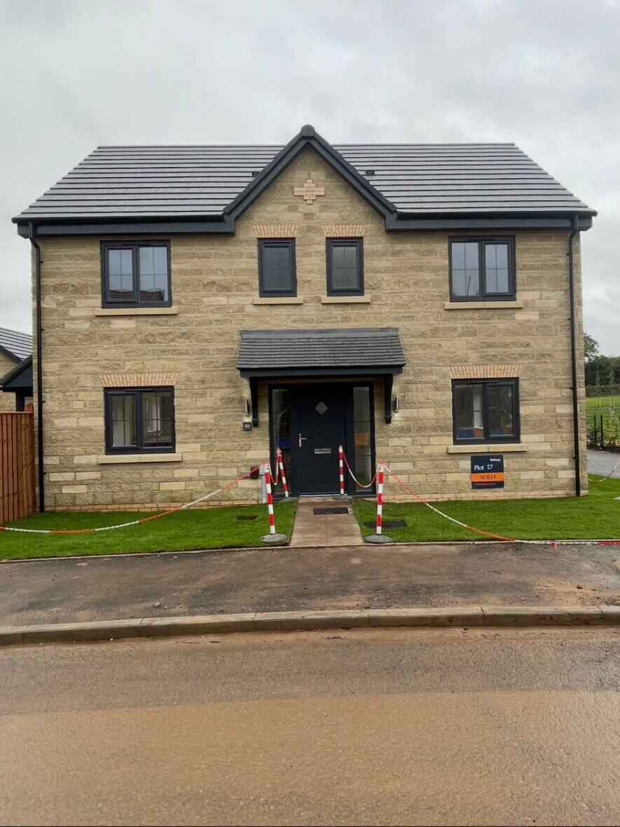 New build stone fronted detached house with slate roof on a housing development