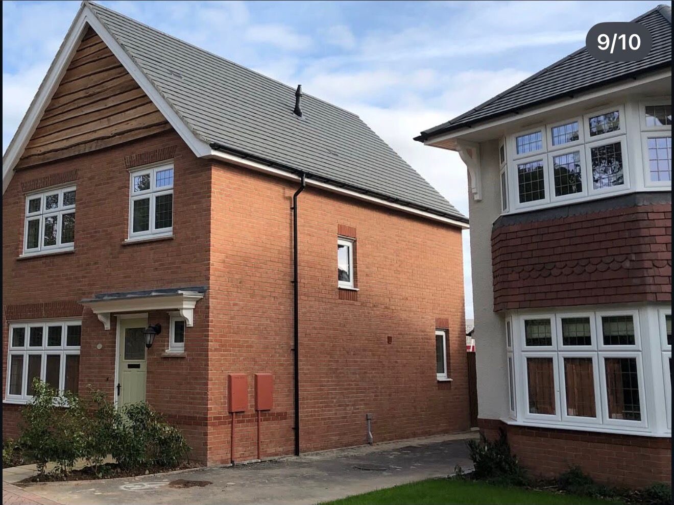 Completed red brick new build detached home beside a bay fronted house