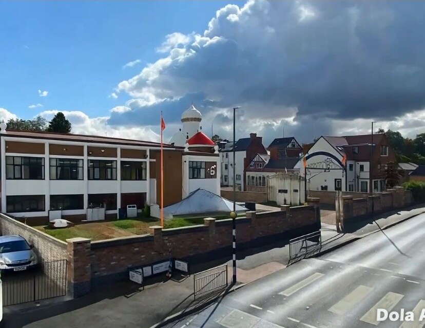 Roadside brick boundary wall with blue brick plinth and stone copings to a community building