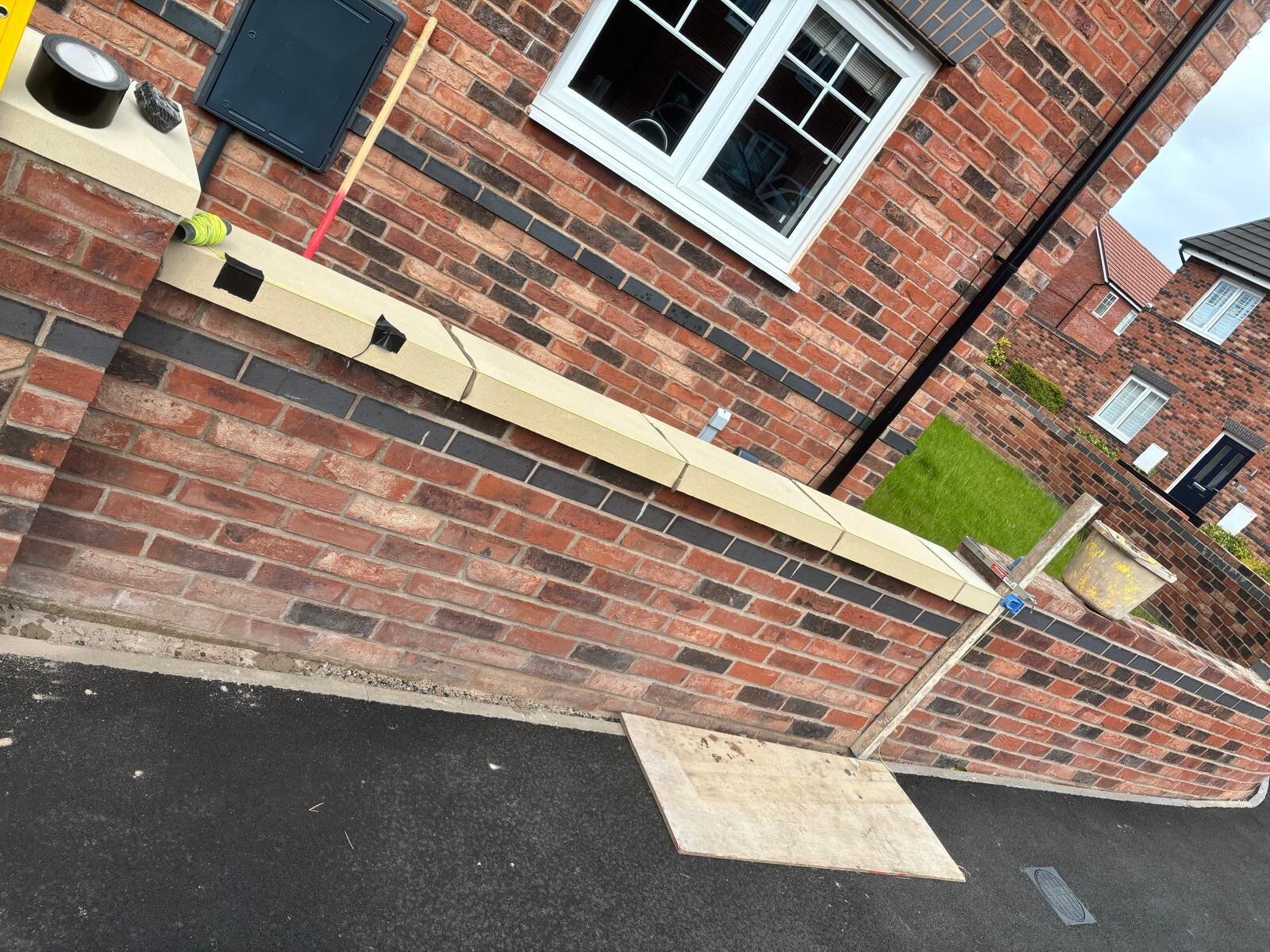 Red brick boundary wall with blue brick banding and cast stone coping laid alongside a new build home
