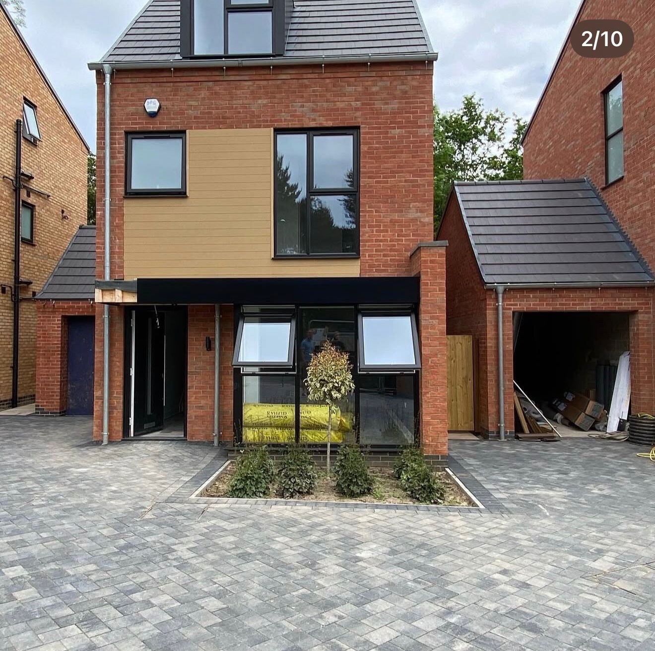 Completed red brick new build home with cladding panel, canopy and detached garage