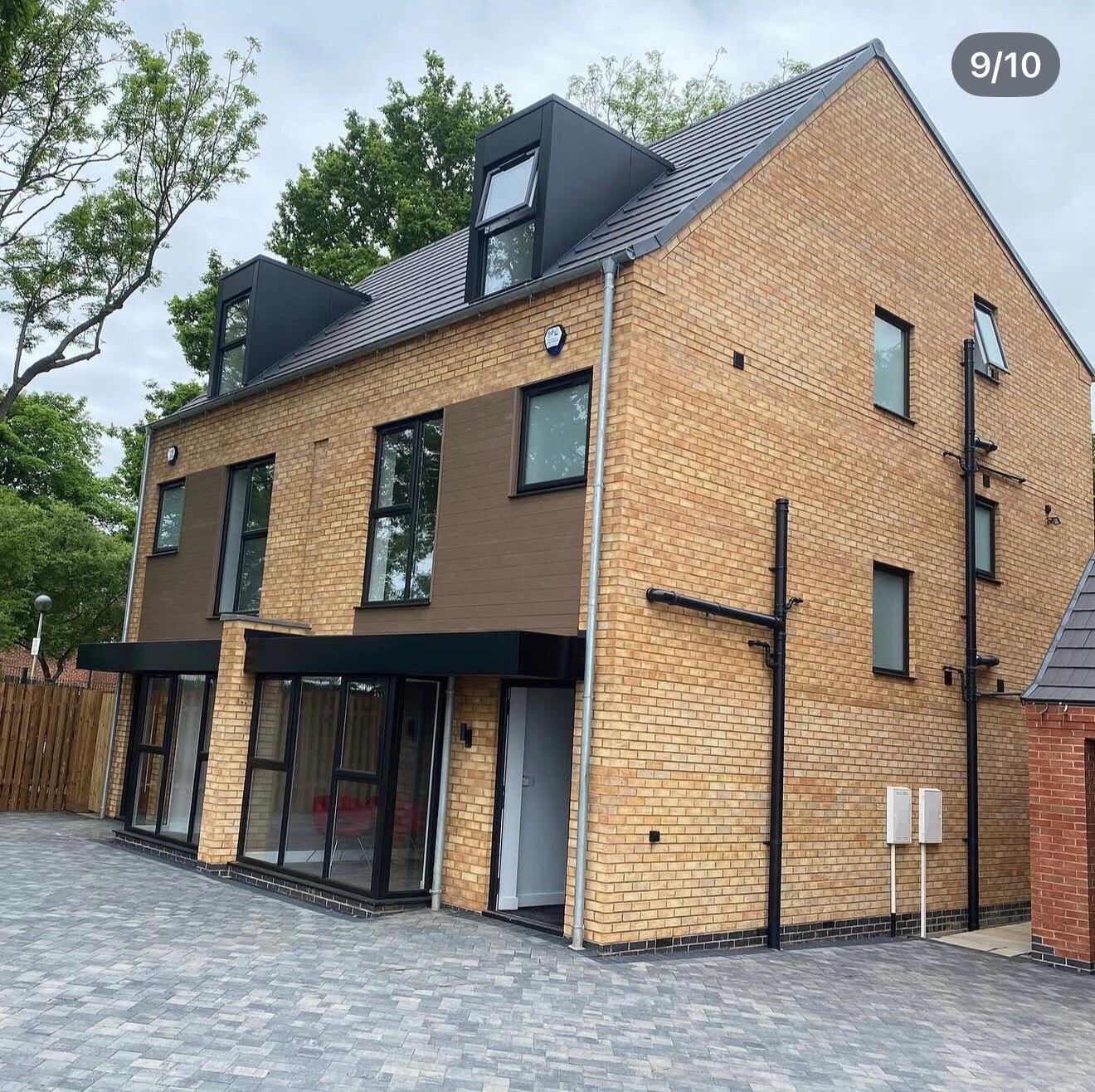 Corner view of a completed buff brick new build townhouse with dormers and cladding panels