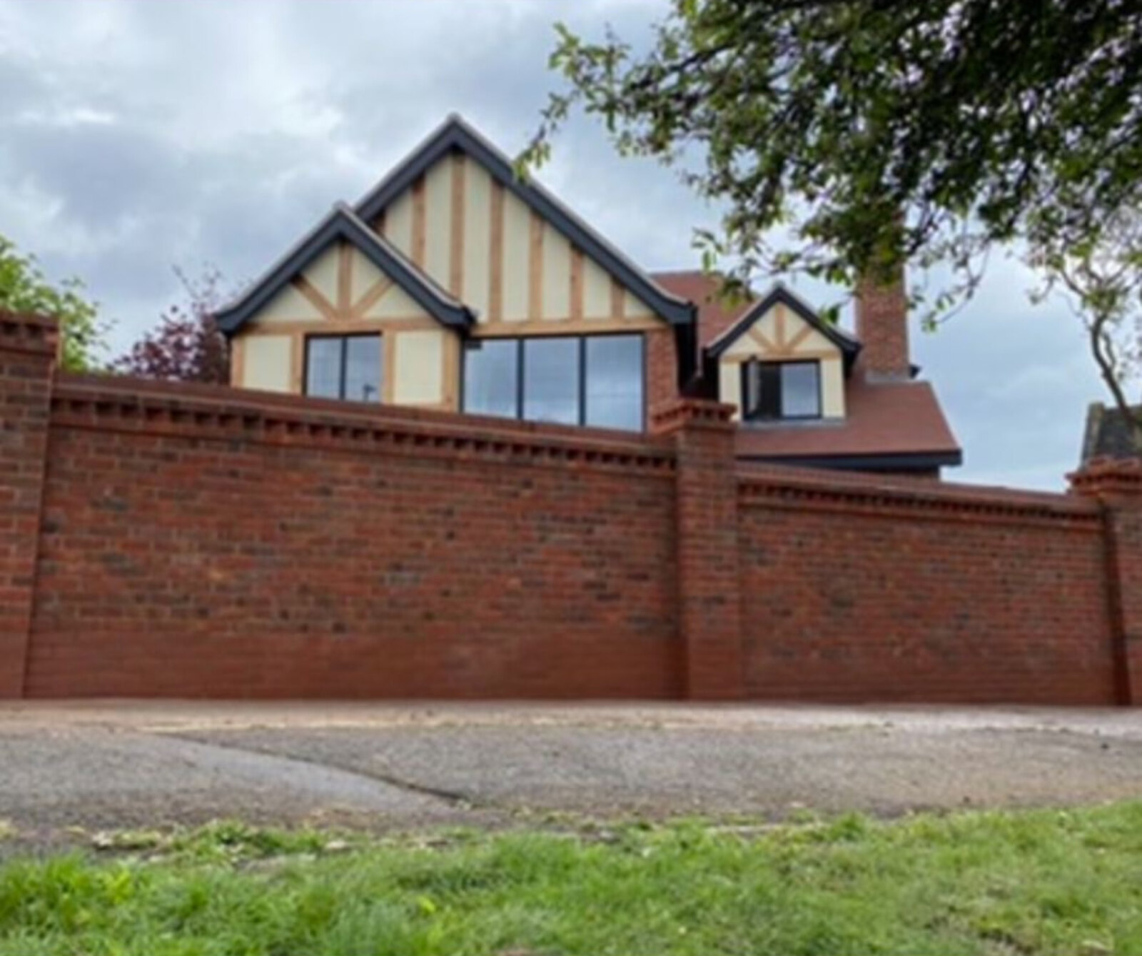 Completed red brick boundary wall with dentil detail in front of a newly built Tudor style house