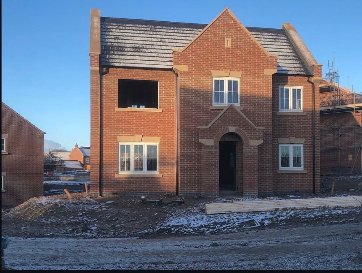 New build detached red brick house with arched entrance, stone details and feature gable
