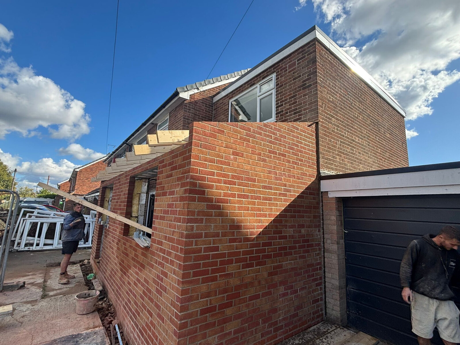 Bricklayers building a two storey extension corner in matching red brickwork