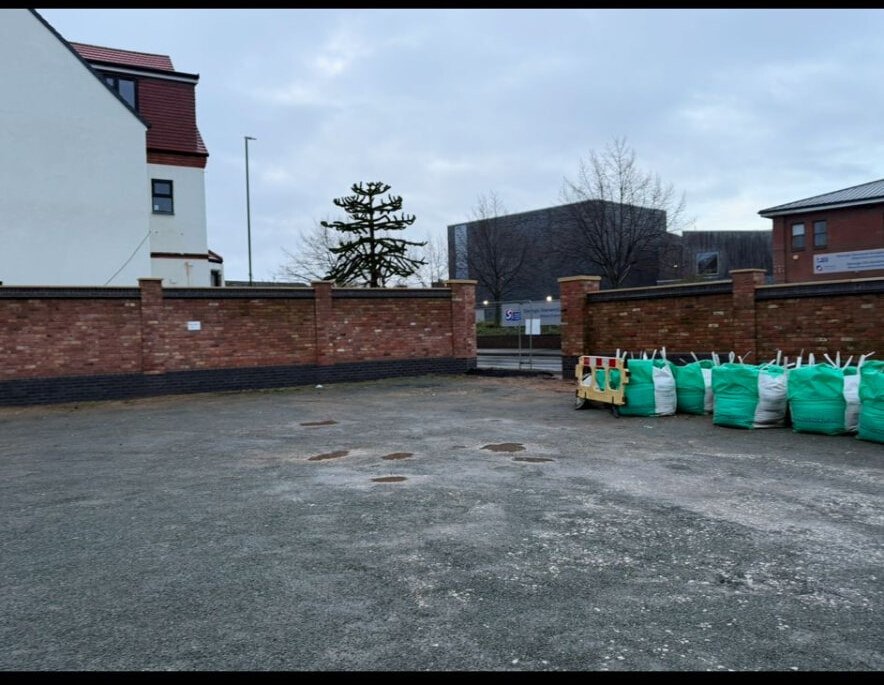 Brick boundary wall with piers and blue brick plinth enclosing a car park
