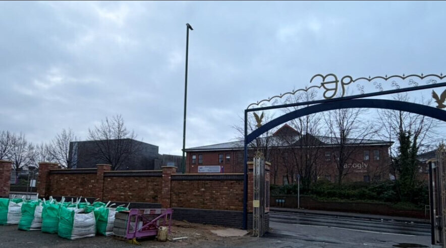 Red brick boundary wall and piers built alongside a decorative site entrance gateway