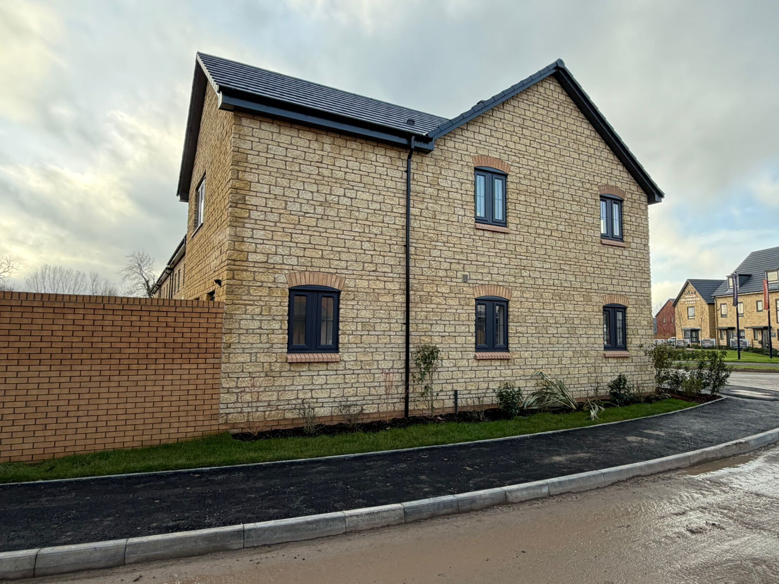 Detached new build in reconstituted stone with brick arch heads and boundary brick wall