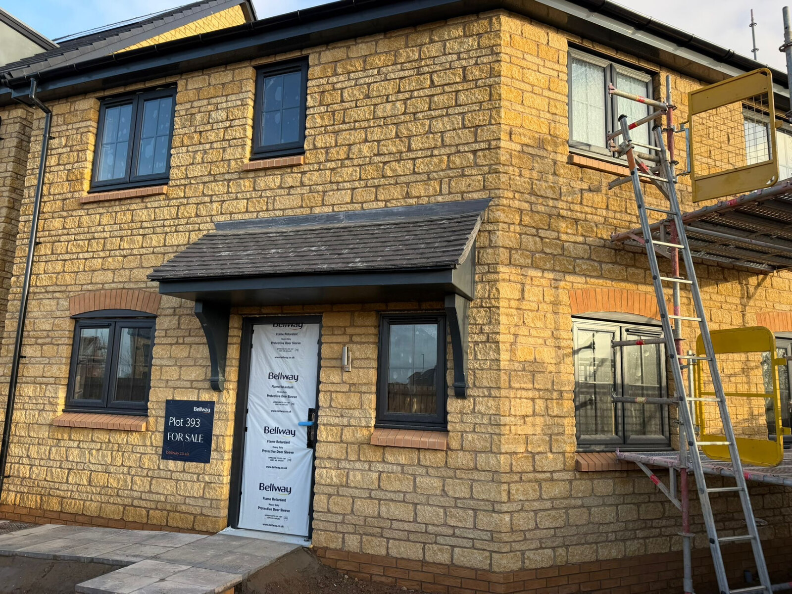 New build corner elevation in reconstituted stone with canopy porch and brick heads
